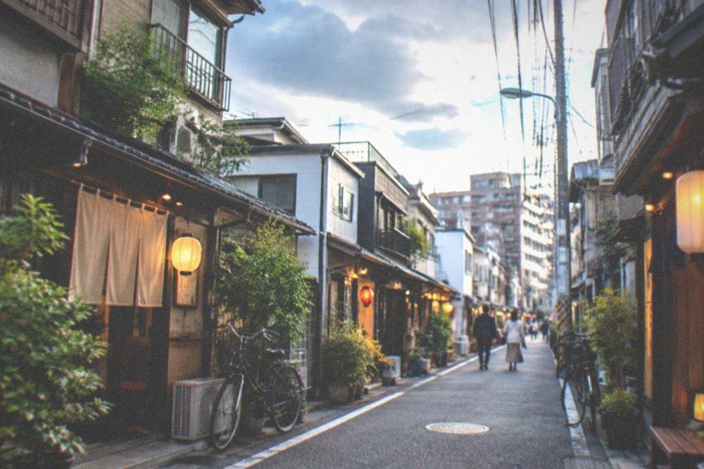 A narrow residential street in Daimyo with small lit bar entrances on both sides