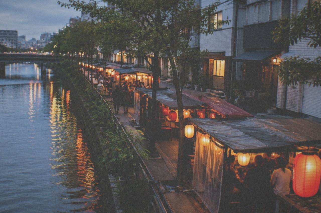 Evening lanterns glowing along a narrow street of food stalls beside a river