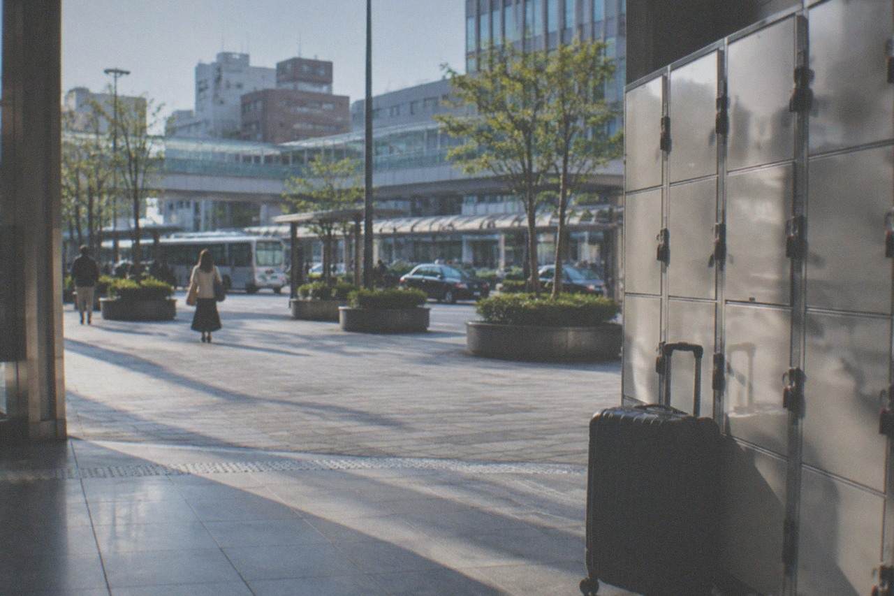 Rows of silver coin lockers along a bright station concourse with a suitcase standing in front of them