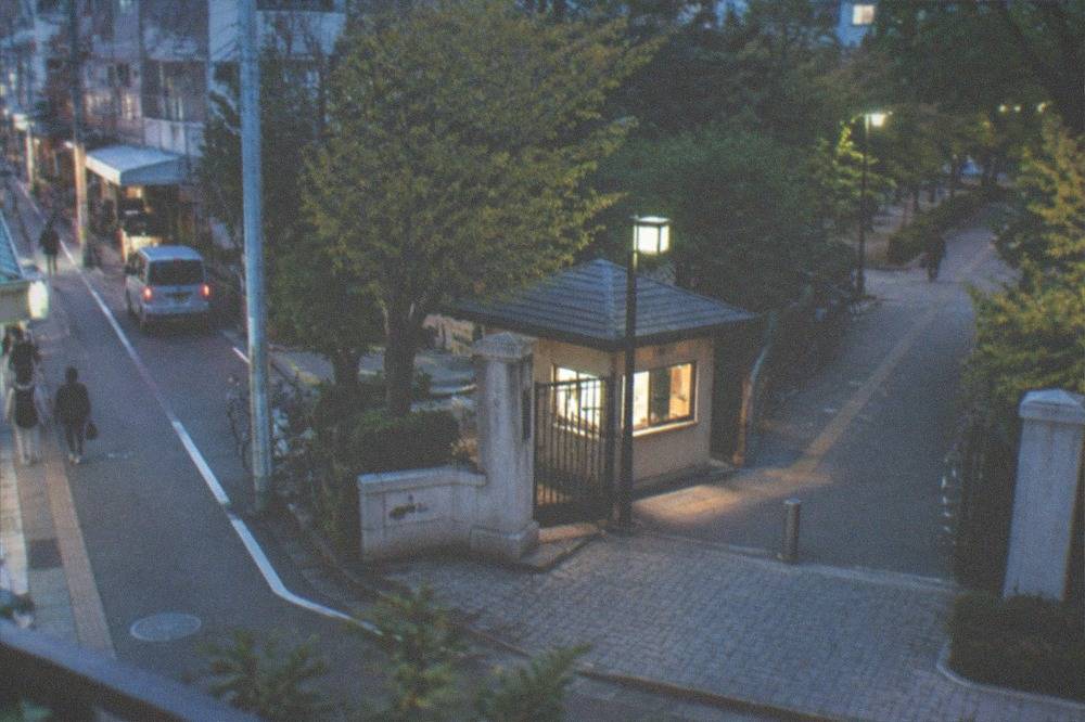 A park entrance gate with a small ticket booth beside a cycle path and trees