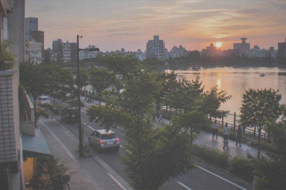 A city skyline of mid-rise buildings seen across a park lake at dusk