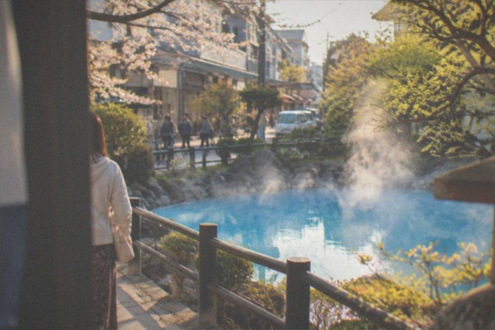A steaming cobalt blue hot spring pond surrounded by garden trees