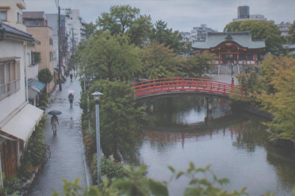 An arched red bridge crossing a pond toward a shrine building
