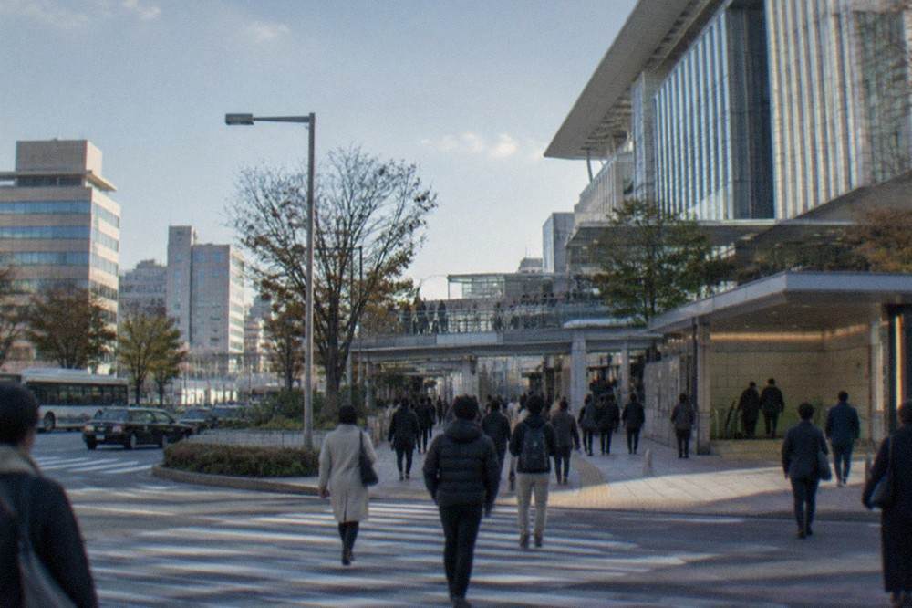 Busy pedestrian crossing with office towers and a subway station entrance in daylight