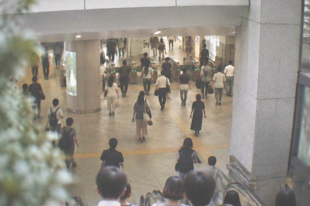 Subway station concourse with fare gate signs and commuters moving through a bright tiled hall