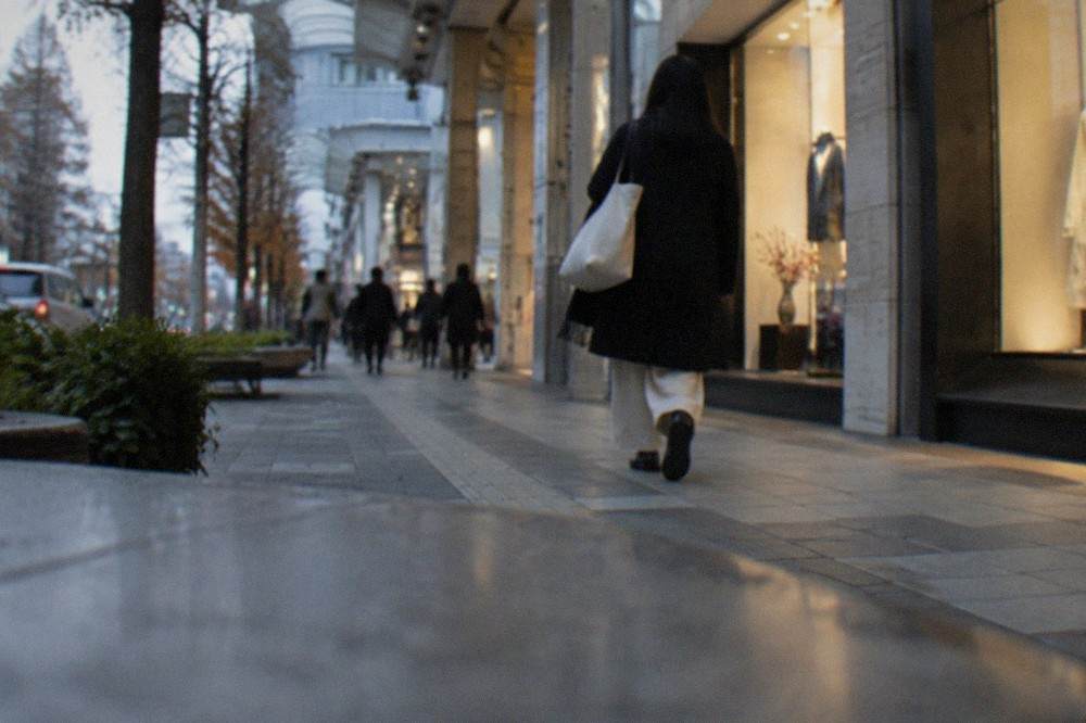 A person walking alone past illuminated shopfronts in a downtown Fukuoka arcade at dusk