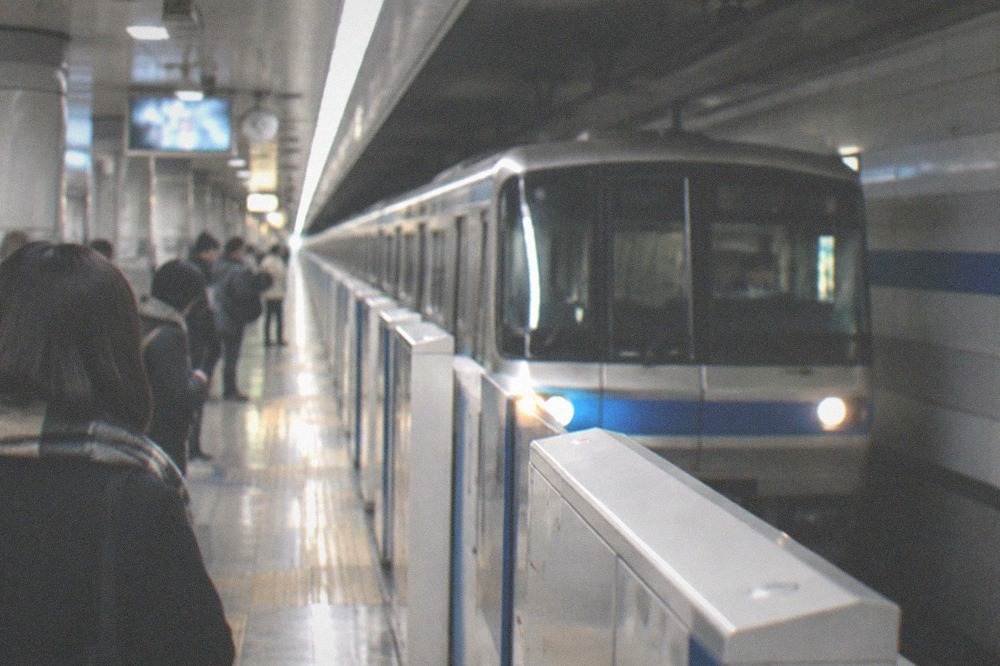 A subway platform in Fukuoka with a train arriving and clear signage