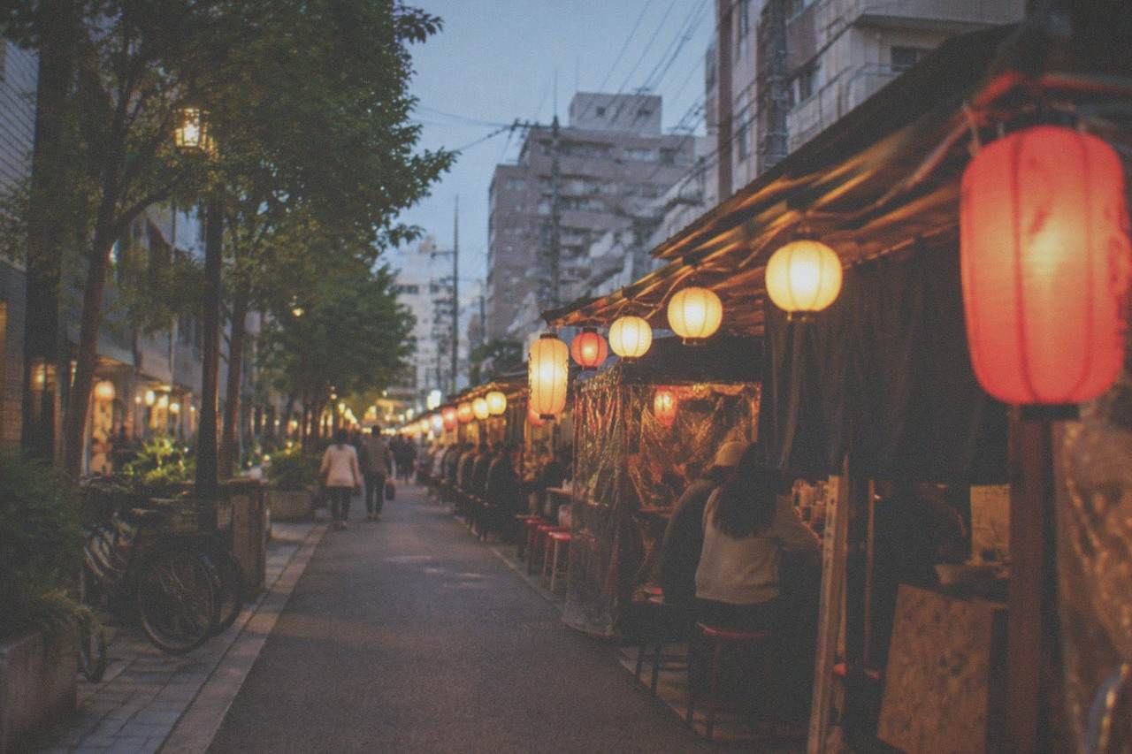 Evening view of a narrow street in Fukuoka with lanterns glowing above small food stalls