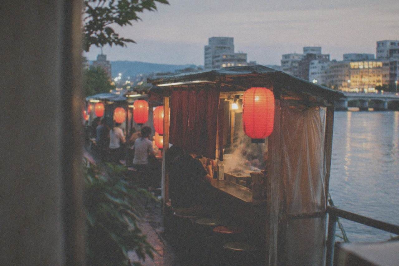 Red lanterns glowing above a row of street food stalls beside a river at night