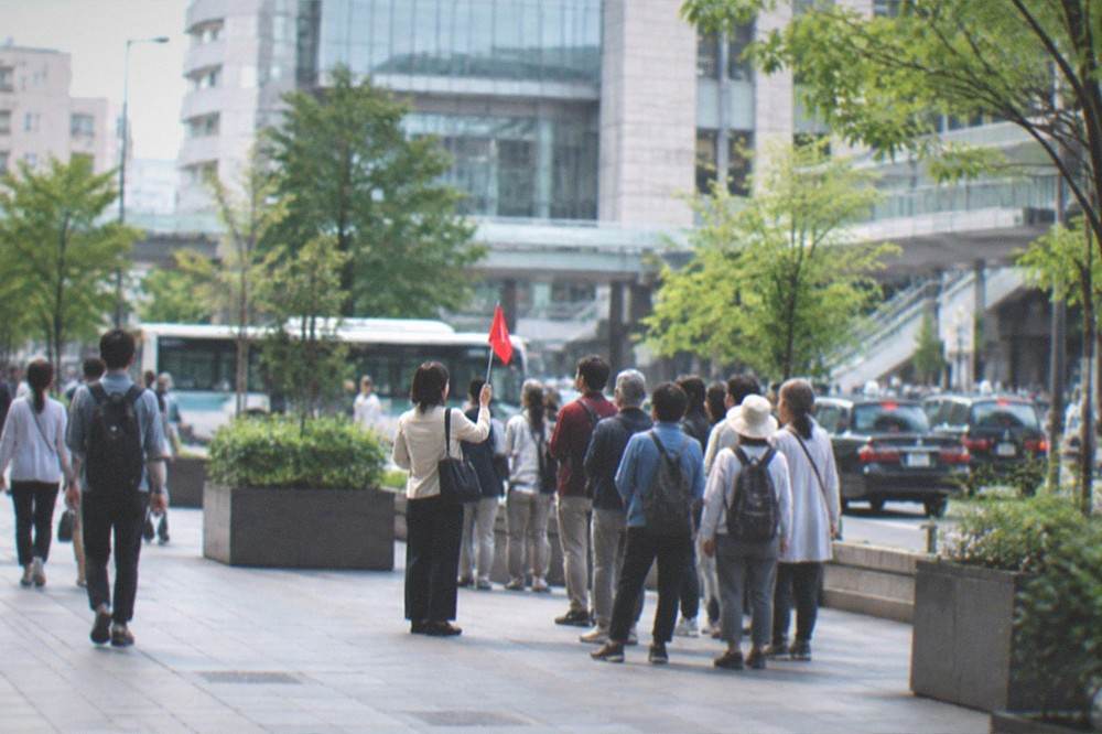 A guide holding a small flag greeting a group near a station exit in Fukuoka