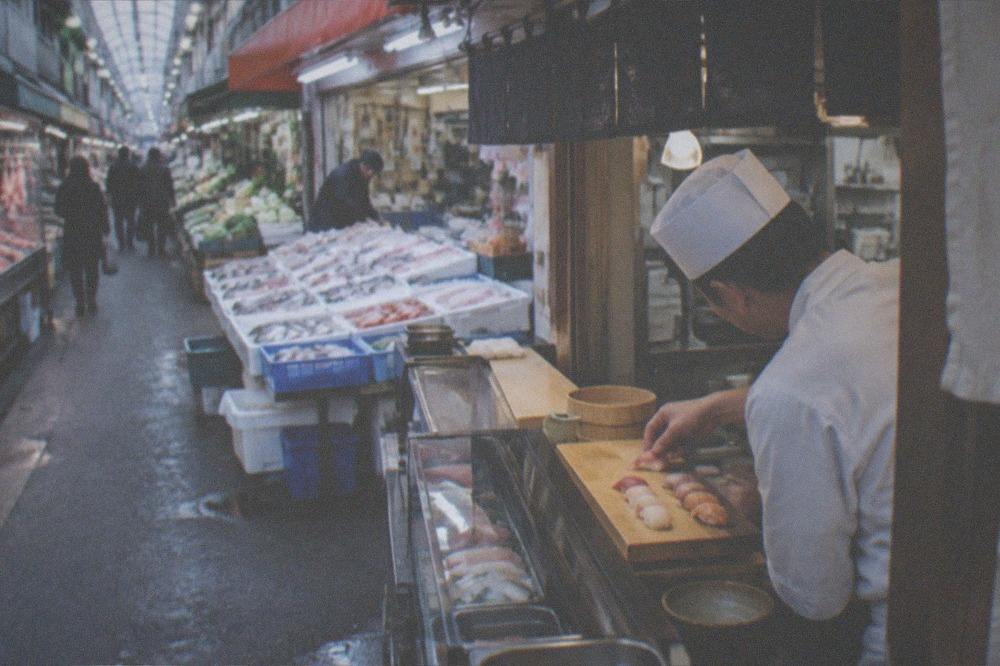 A chef placing a piece of nigiri onto a wooden serving block at a counter