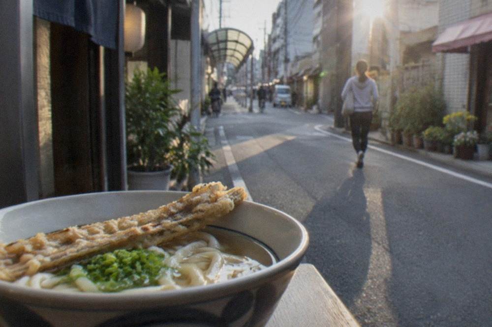 A bowl of Hakata udon with a crisp burdock tempura resting on soft noodles in clear broth
