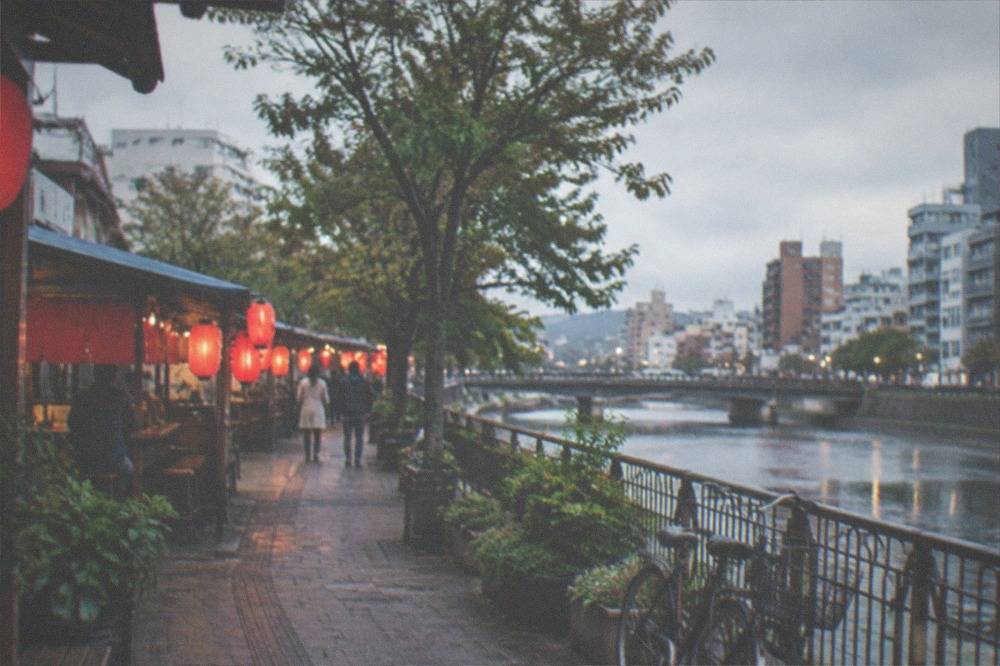 Small open-front food stalls with red lanterns glowing along a riverside walkway