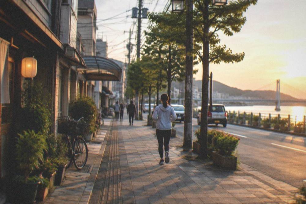 Sunset over a Japanese harbour city with a bridge, calm water and warm light on the buildings