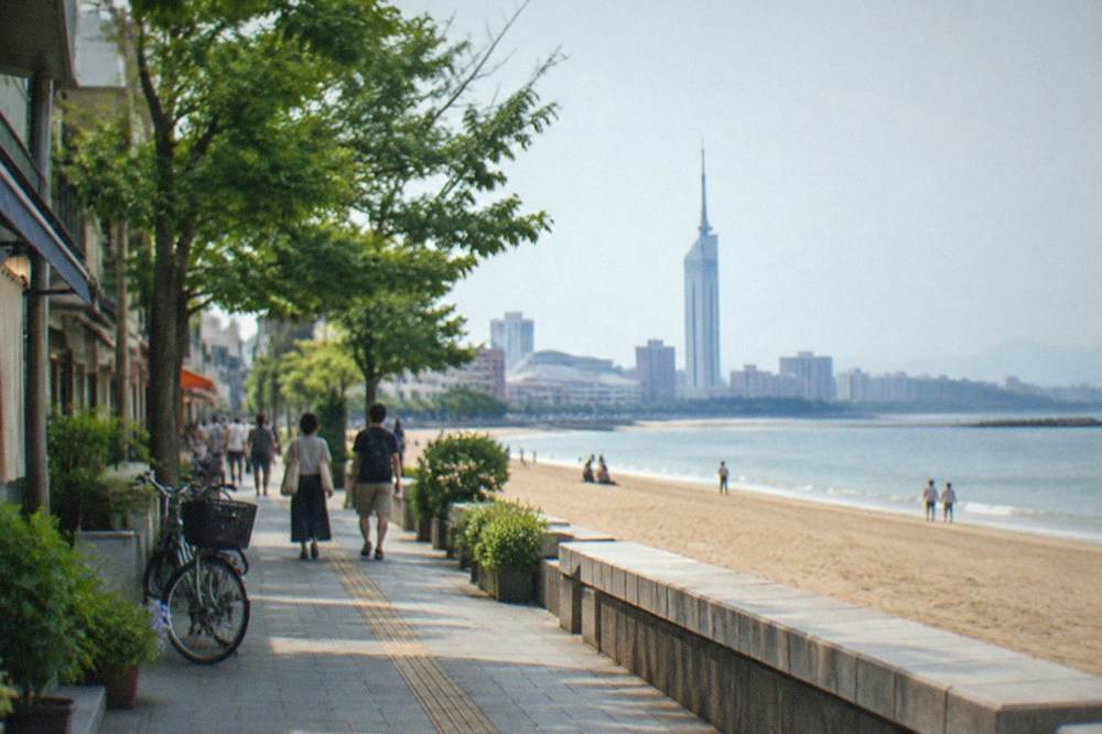 A tall seaside observation tower above a wide sandy beach with calm water and a long promenade.