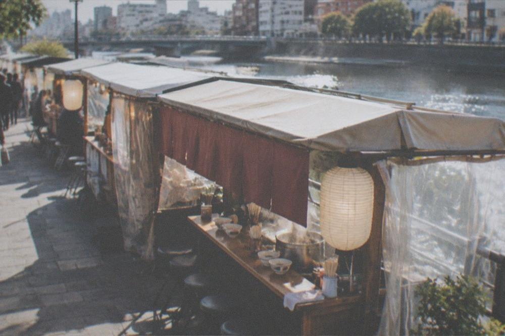 Bowls and chopsticks laid out on a wooden stall counter beside a steaming pot