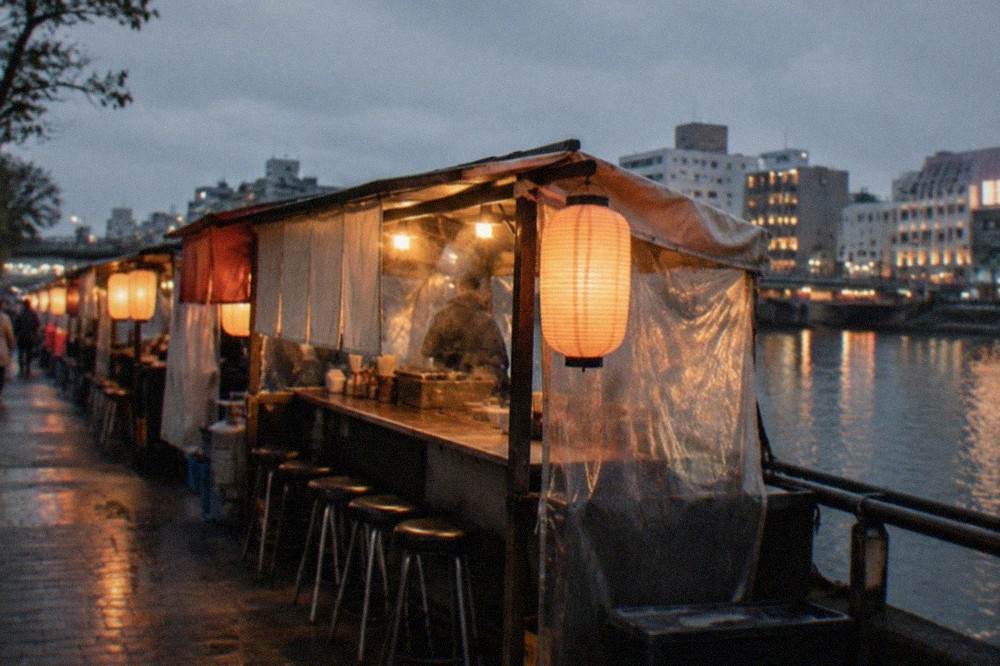 Riverside food stalls glowing with warm lantern light beside a dark canal in a city entertainment district