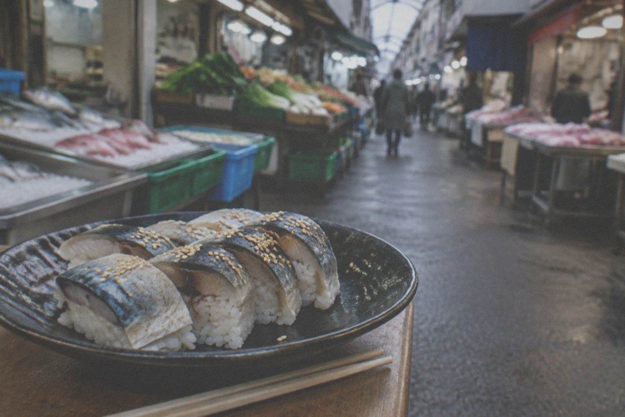 slices of sesame coated mackerel sushi arranged on a dark ceramic plate with chopsticks