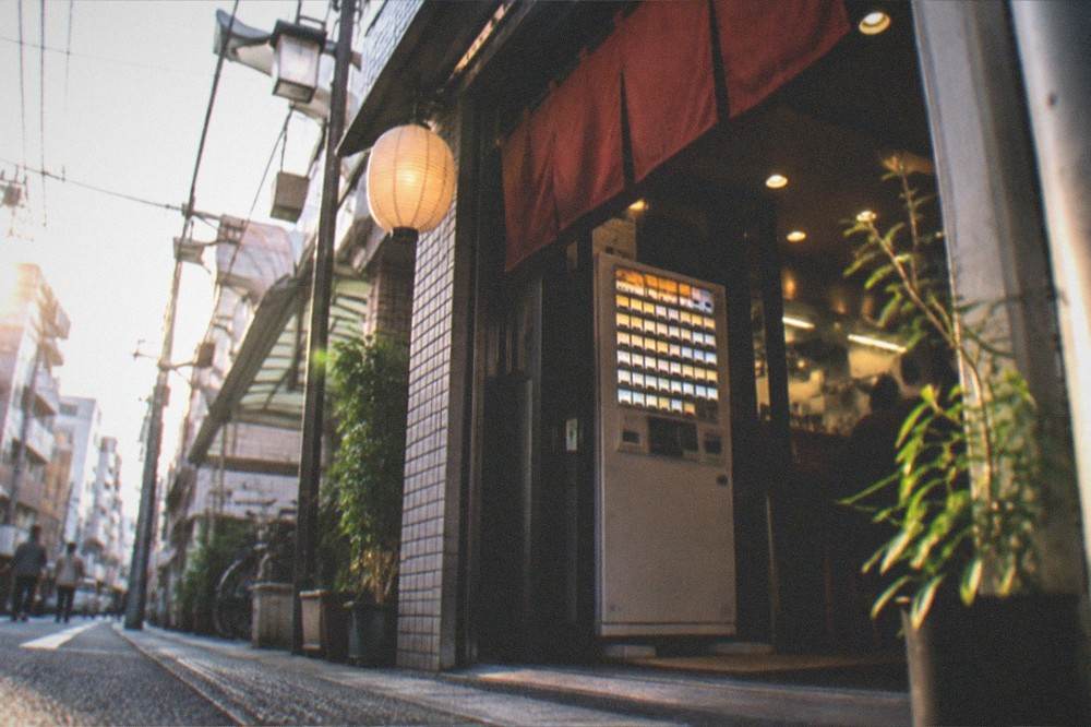 A ramen shop ticket machine with illuminated buttons inside a small shop entrance