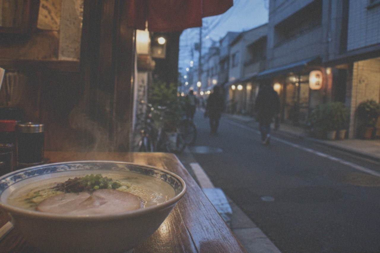 A steaming bowl of tonkotsu ramen with thin noodles and sliced pork on a wooden counter