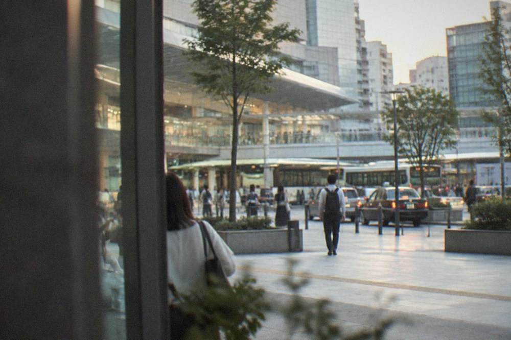 A busy station forecourt with glass towers behind it in the evening