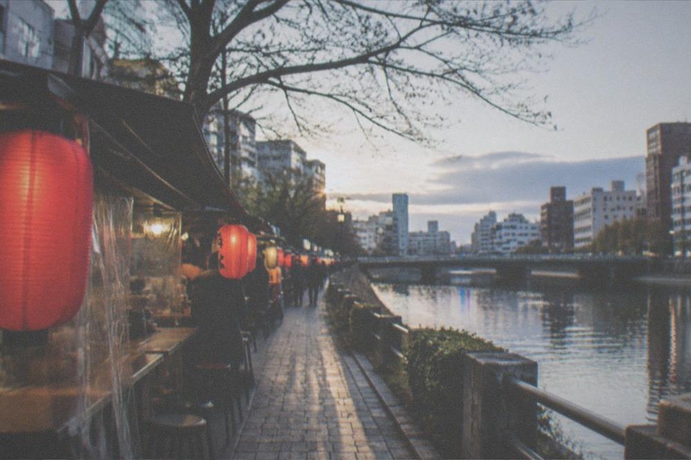 Food stalls with red lanterns glowing along a riverside at night