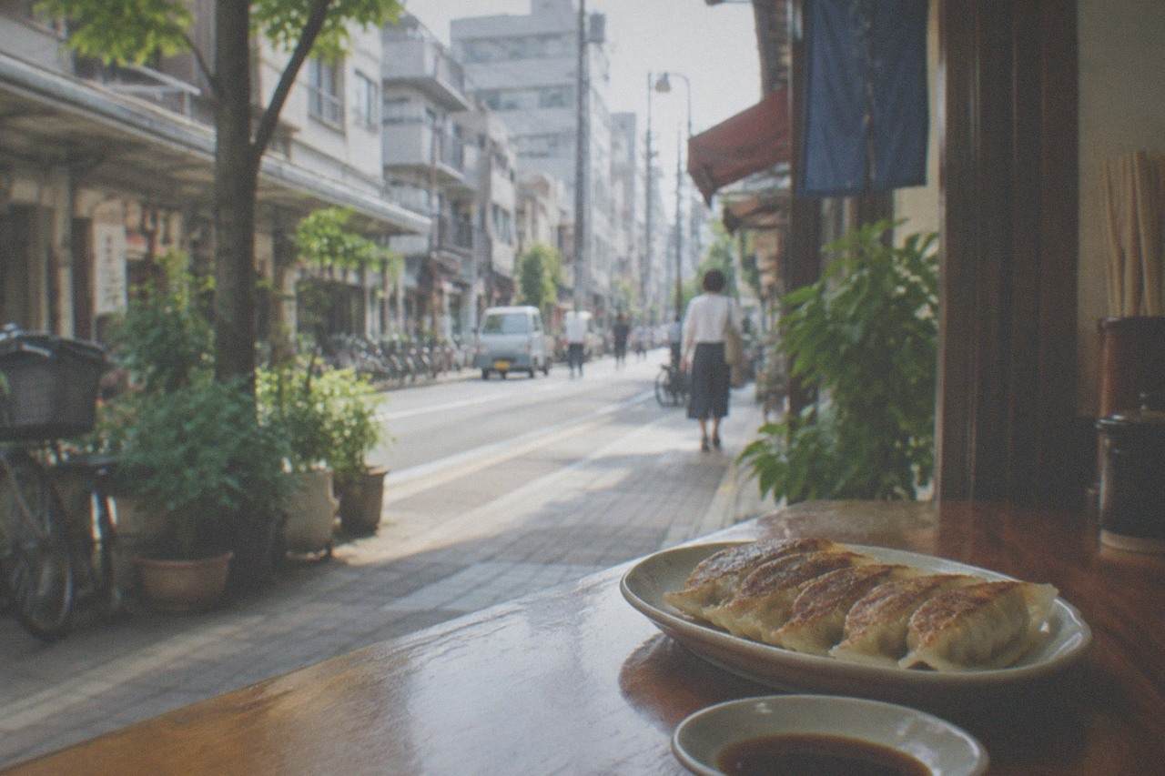 A plate of small pan-fried dumplings on a wooden counter beside a small dish of dipping sauce