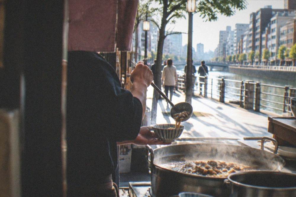 Close view of a server ladling broth and offal from a hot pot into a small bowl