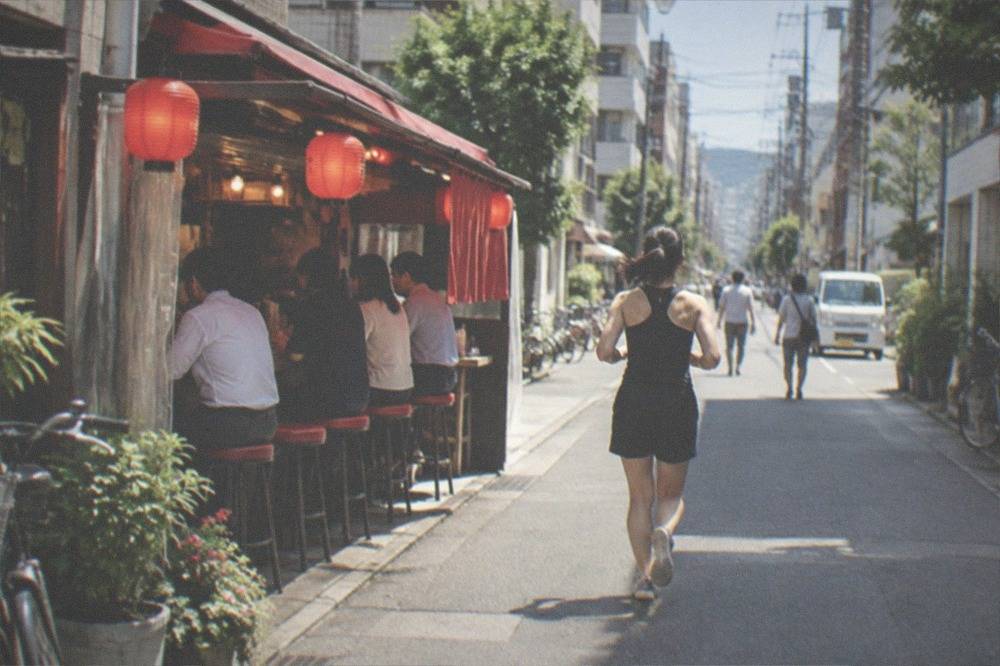 A crowded street food stall with red lanterns and customers seated at a narrow counter