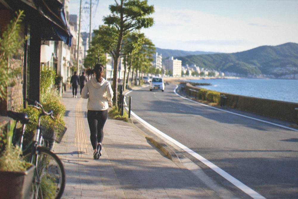 A coastal road curving along a blue sea with green hills behind it