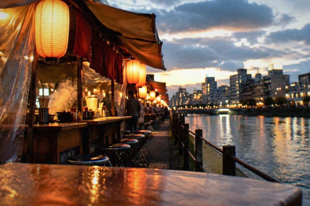 Lanterns glowing above food stalls beside a river at night