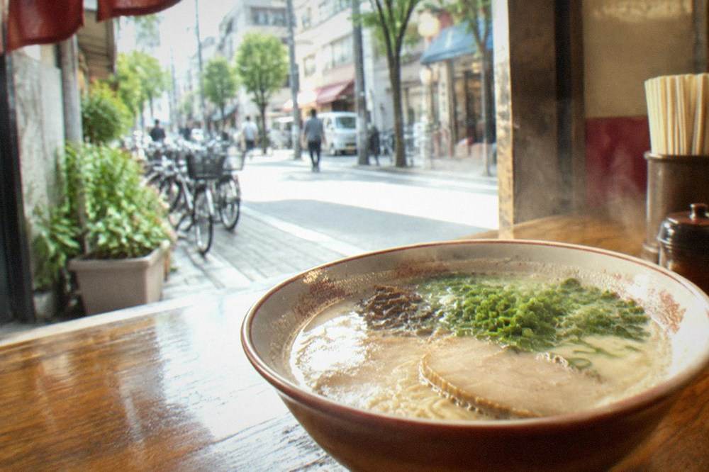 Steaming bowl of tonkotsu ramen with thin noodles and sliced pork on a wooden counter