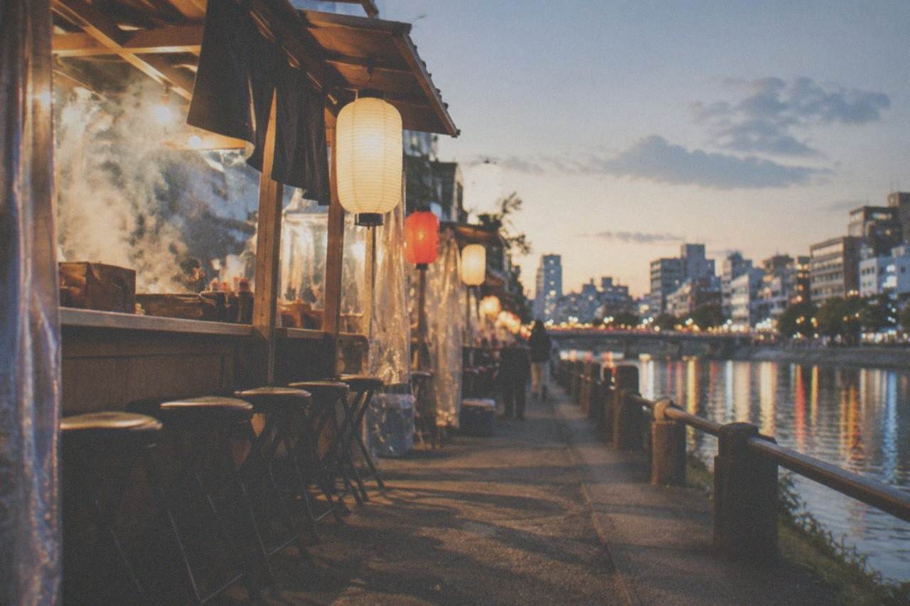 Evening lantern light reflecting on the Naka River beside rows of yatai food stalls in Nakasu
