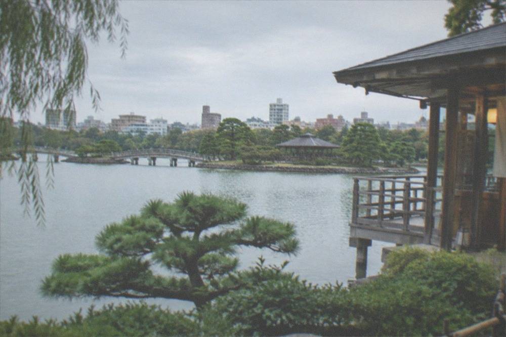 Pond garden with clipped pines and a wooden pavilion beside the Ohori Park lake