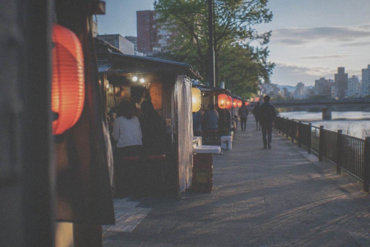 Illuminated food stalls lined along a riverfront street in a Japanese city at night