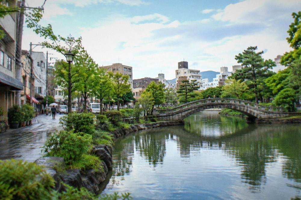 Calm pond reflecting trees and a stone bridge in a large Japanese park