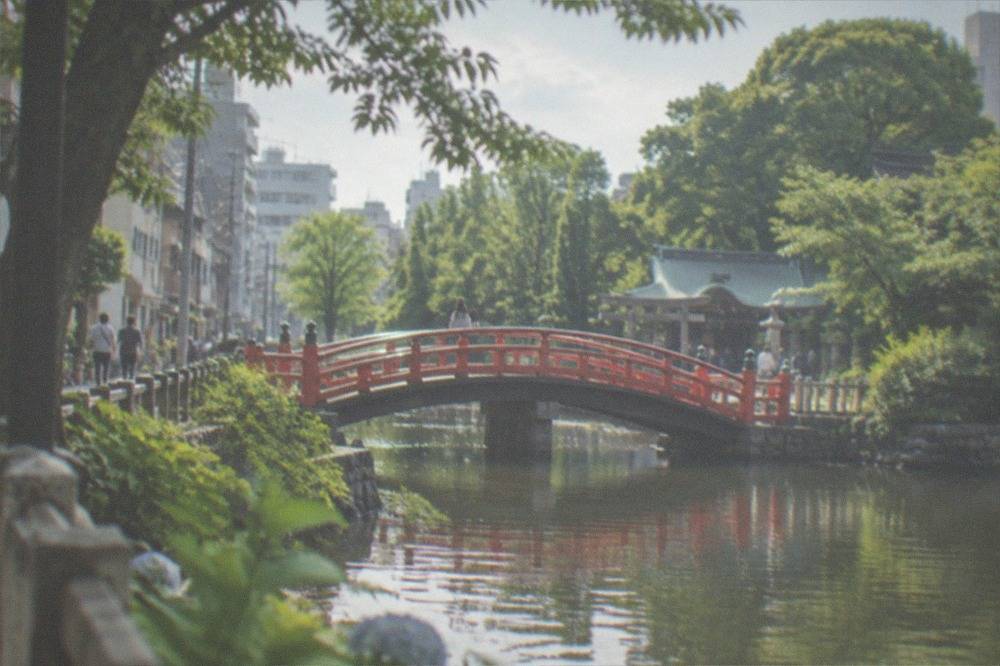 Red arched bridge over a pond leading to a shrine among trees