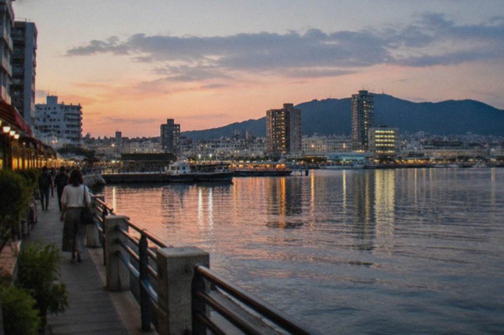 Hakata Bay at dusk with city lights reflecting on the water and hills across the bay
