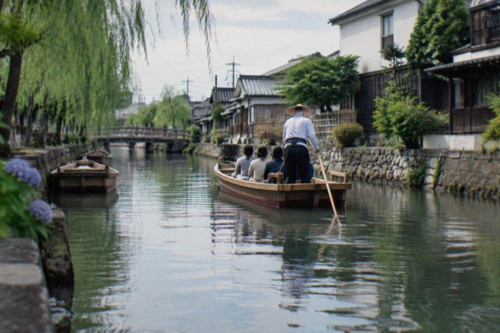 A canal boat drifting between low wooden houses in Yanagawa on a calm morning